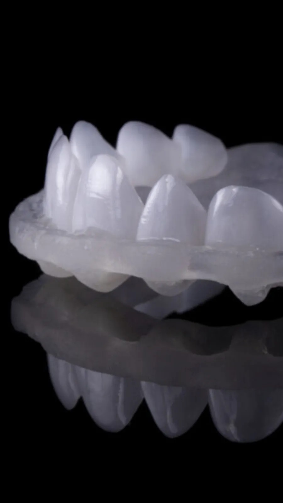 A finished printed dental appliance photographed on a reflective black surface